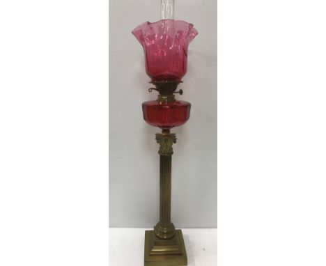 A Victorian brass corinthian column table lamp with cranberry glass reservoir and shade 83 cm high not including chimney