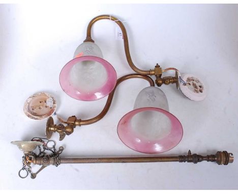 A pair of early 20th century brass single sconce wall light fittings, each having a cranberry tinted etched glass bell shaped