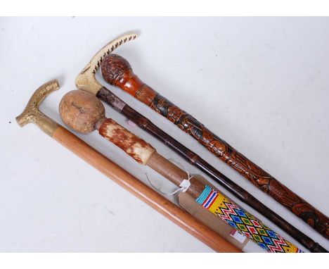 An African staff, having a coloured bead and hide collar; together with a carved walking stick; one other brass topped walkin