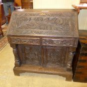 A late Victorian profusely carved oak bureau the fall front above drawers and cupboards flanked by