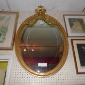 A C19th wall mirror the original oval bevelled plate within carved giltwood frame with carved