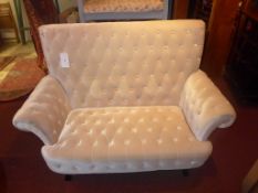 A two seater settee upholstered in buttoned ivory velour on ebonised supports.