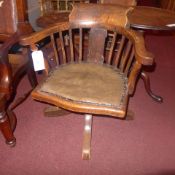 A 1930`s oak desk chair upholstered in leather and raised on swivel supports