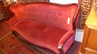 A Victorian walnut four seater settee of serpentine outline and upholstered in rouge buttoned