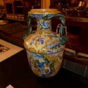 A Majolica vase with twin serpent form handles glazed Classical battle scenes and cherubs