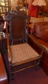 An oak Carolean design open armchair with carved detail and a caned seat raised on turned supports
