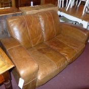 A contemporary two seater sofa upholstered in tan leather and raised on black supports