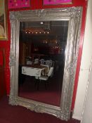 A rectangular wall mirror of large size the bevelled plate within silver painted and ornately carved