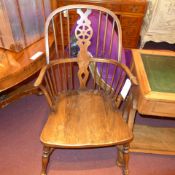 A C19th elm windsor elbow chair with pierced wheel and stick back above solid seat raised on
