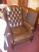 A Georgian style wing back chair upholstered in brown buttoned leather with studded detail on