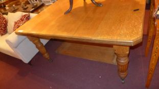 A Victorian oak extending dining table with one extra leaf raised on reeded supports and castors