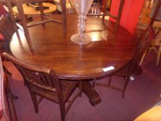 A large circular teak dining table raised on a heavy pedestal terminating in a tri-form base