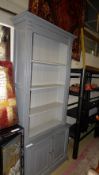 A distressed painted bookcase the open shelves above cupboards