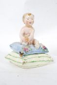 An unusual 20th century porcelain figurine of a cherub / small child raised on a cushion base.