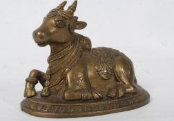 A 20th century Indian brass religious ornament of a seated sacred cow raised on an oval plinth