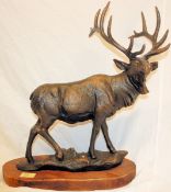 A large bronze effect cast iron statue of a stag. Standing proud with large horns, on a wooden