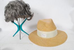 A 1970's green plastic wig stand together with wig and a straw hat