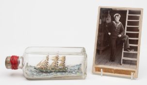 An early 20th century photograph of a sailor, together with a ship in a bottle:,