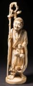 A Japanese carved ivory okimono of a bearded figure: with staff in one hand and gourd in the other,
