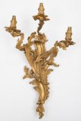 A set of four gilt brass three branch wall lights: of scrolling form with foliate decorated nozzles