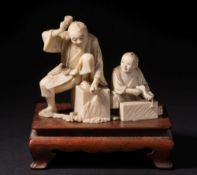 A Japanese carved ivory okimono of a stone mason and his apprentice: both working on stone blocks,