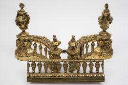A pair of gilt brass chenets: of scroll form surmounted with neo-classical urns and  ram's head