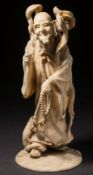 A Japanese carved ivory okimono of a bearded figure: in flowing robes holding prayer beads,