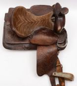 A hand tooled leather Western style trail saddle:, acorn embossed decoration and wooden stirrups.