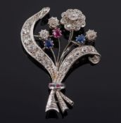 A diamond, sapphire and ruby mounted floral spray brooch: with single flower head, ribbons and buds,