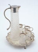 A silver mounted cut glass liqueur jug with four silver mounted tot glasses:  on a silver pie crust