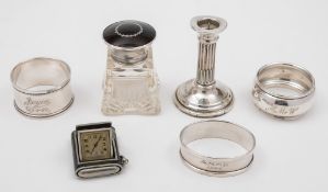 An Art Deco period folding travelling timepiece: three silver serviette rings,