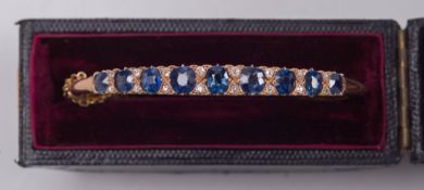 A gold, sapphire and diamond hinged bangle: with graduated, oval sapphires between old-cut diamonds,