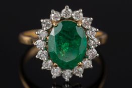 An emerald and diamond oval cluster ring:, the oval emerald within a surround of circular,