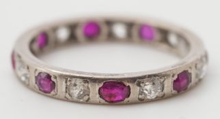 A white metal, ruby and diamond eternity ring: set with oval rubies and circular,