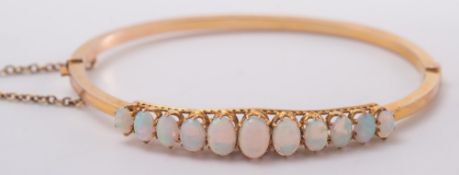 A gold and graduated opal hinged bangle: with safety chain.