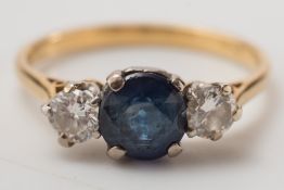 An 18ct gold, sapphire and diamond three stone ring:, the circular sapphire in four claw setting,