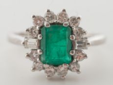 An emerald and diamond cushion-shaped cluster ring: with central 'emerald-cut' emerald,