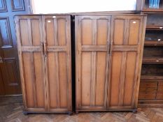 A pair of reproduction oak wardrobes, the panel doors enclosing hanging space and shelves,