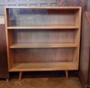 A modern hardwood bookcase of three shelves with glazed sliding doors and turned tapering legs,