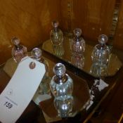 A collection of three glass perfume bottles with yellow pink and blue and mirrored trays