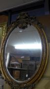 A wall mirror the oval bevelled plate in carved gilded frame