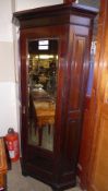 An Edwardian mahogany corner cupboard with bevelled mirrored door enclosing coat hooks raised on