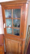 An antique pine corner cabinet fitted glazed panel door above further panelled door enclosing