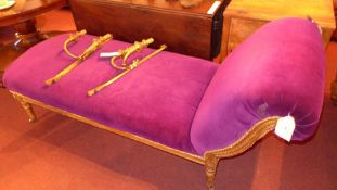 An antique chase longue, upholstered in purple velour with an ornate giltwood frame raised on carved