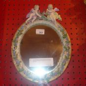 A C19th Meissen porcelain table mirror the oval plate within flower encrusted frame with cherub