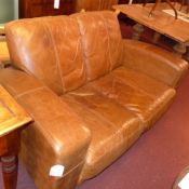 A contemporary two seater sofa upholstered in tan leather and raised on black supports