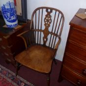 A C19th elm windsor elbow chair with pierced wheel and stick back above solid seat raised on