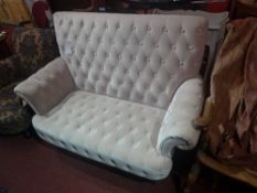 A two seater settee upholstered in buttoned ivory velour on ebonised supports.
