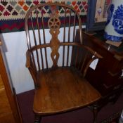 A C19th elm windsor elbow chair with pierced wheel and stick back above solid seat raised on