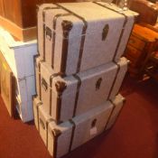 A set of three grey fabric clad storage trunks of graduating size
